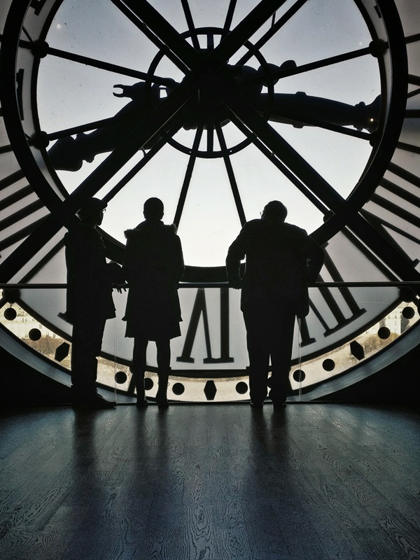 sillouettes of two men and a woman in front of a clock
