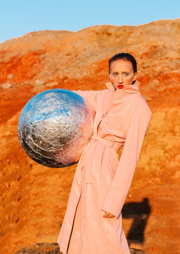 Woman in a trench coat posing while holding a foil covered ball